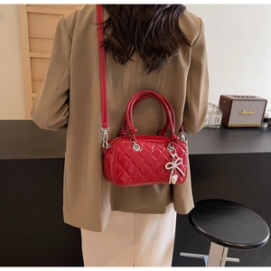 Detail of red quilted faux leather handbag with rhinestone bow pendant and handle