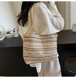 Detail of striped woven straw tote bag with metal button closure and fabric shoulder straps