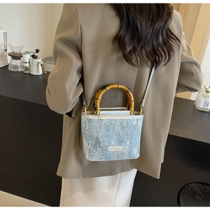 Detail of sequined denim bucket bag with bamboo handle worn as a crossbody bag