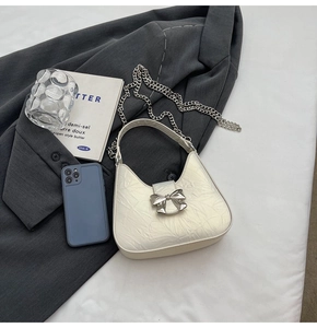 Détail d'un sac demi-lune plissé blanc avec fermoir nœud en métal argenté et bandoulière