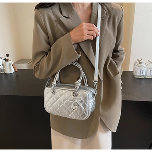 Silver quilted crossbody bag with sequined bow detail and heart pendant on a model