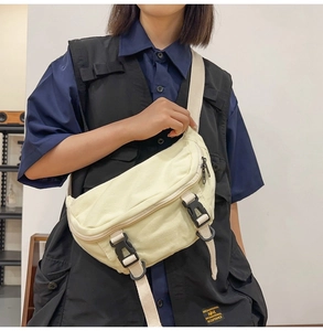 Detail of beige canvas crossbody chest bag featuring dual black buckles and metal zipper