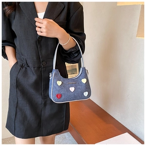 Detail of blue denim shoulder bag featuring colorful heart patches and metal logo