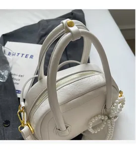 Gros plan d'un sac crème avec double fermeture éclair dorée et pendentif noeud perle