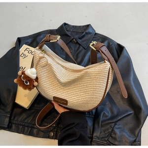 Detail of crescent straw shoulder bag with brown leather trim and cute plush charm on black coat
