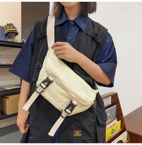 Detail of off-white canvas chest bag featuring black quick-release buckles and textured fabric