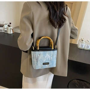 Detail of blue textured bucket bag with a bamboo handle and long black shoulder strap