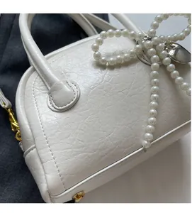 Détail du sac coquillage blanc avec texture plissée, pendentif perle et métal doré