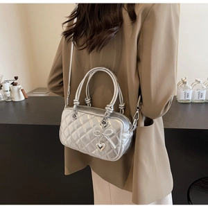 Detail of silver quilted crossbody bag with heart pendant worn with a brown blazer