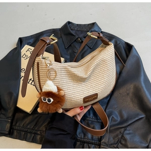 Detail of raffia crescent bag featuring leather trim and a brown plush monster charm