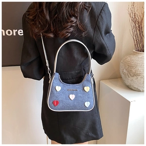 Detail of blue denim shoulder bag featuring colorful heart patches and a top handle