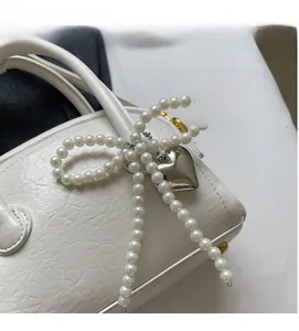 Détail du sac à main en cuir blanc avec nœud en perles et pendentif cœur argent