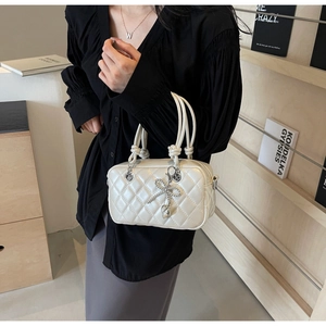 Detail of white quilted crossbody bag featuring a rhinestone bow pendant and silver hardware