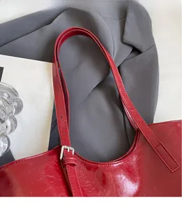 Detail of red glossy leather tote bag with adjustable silver buckle on smooth shoulder strap