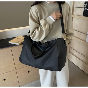 Détail d'un grand sac de voyage en nylon noir avec poignée renforcée et bandoulière sur mannequin