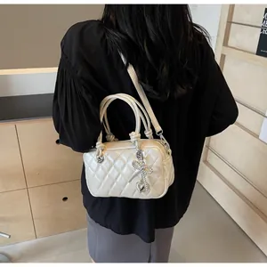 Close-up of cream quilted crossbody bag with silver bow and heart charms on wooden backdrop