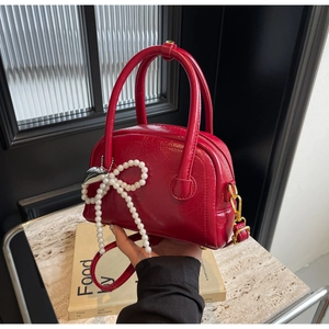Détail du sac rouge en cuir verni avec nœud en perles et breloque en forme de cœur