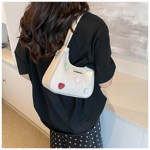 Detail of silver crescent armpit bag featuring colorful 3D heart patches and metal logo