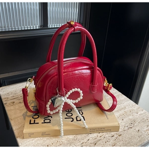Gros plan d'un sac Boston rouge brillant avec un nœud en perles et un pendentif cœur argent