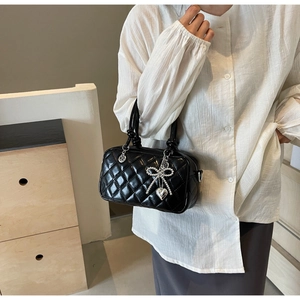 Detail of black quilted crossbody bag featuring silver bow charms and woven handles