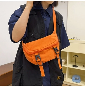 Detail of orange canvas crossbody bag featuring black buckle closures and wide strap