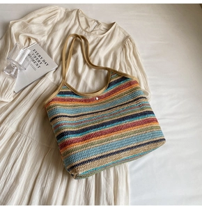 Detail view of colorful striped straw tote bag with snap closure on white dress background