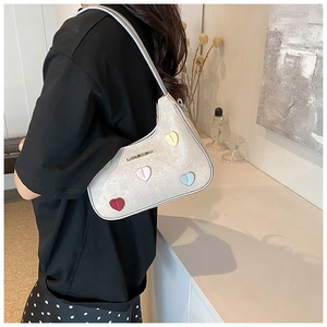 Silver shoulder bag with colorful heart patches shown on a model in a lifestyle setting