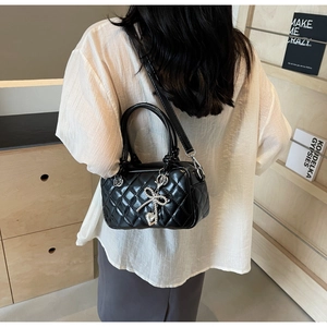 Rear view of a model wearing a black quilted handbag with a silver heart pendant