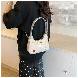 Detail of a chic cream mini hobo bag with colorful heart patches worn as a crossbody