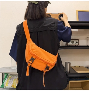 Detail of a bright orange canvas crossbody bag featuring black buckle straps on a model