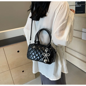 Close-up of black quilted crossbody bag with silver bow heart charm on white shirt