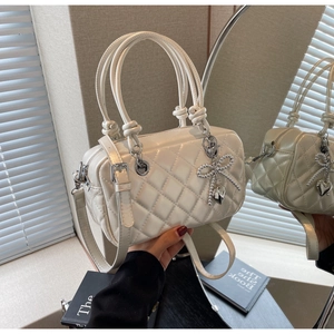 Close-up of quilted cream crossbody bag with bow heart charm and twin handles detail