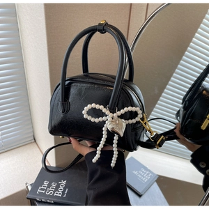 Détail du mini sac verni noir avec nœud en perles et breloque cœur sur la poignée