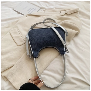 Detailed shot of a navy denim crescent bag with a silver chain on a beige corduroy jacket