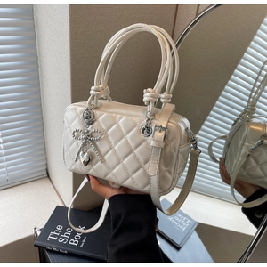 Detail of white quilted handbag with pearl bow charm and glossy leather texture