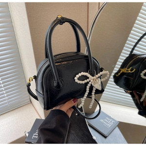 Détail d'un sac à main noir verni avec nœud en perles et pendentif cœur argenté