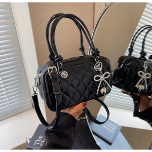 Detail of black quilted crossbody bag with silver bow charm and heart pendant decoration