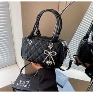 Detailed close-up of a black quilted leather handbag featuring silver heart charm and bow