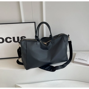 Détail du sac de voyage noir avec poignées renforcées, métal doré et bandoulière