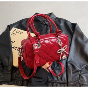 Detail view of red quilted handbag with pearl bow charm and glossy leather texture