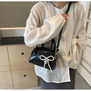Détail du sac en cuir verni noir avec nœud en perles et pendentif cœur argenté