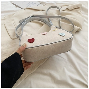 Detail shot of canvas handbag with colorful heart patches and dual straps on bed
