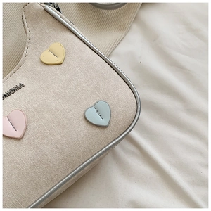 Detail view of beige canvas shoulder bag featuring multi-colored stitched leather hearts