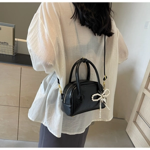 Détail du sac à main noir brillant avec nœud en perles et finitions dorées