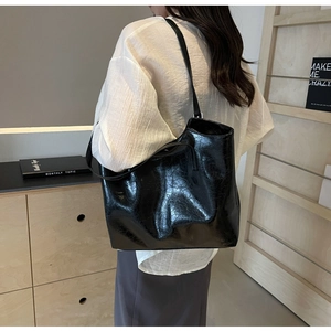 Side view of a large black crinkled patent leather tote bag on a model's shoulder