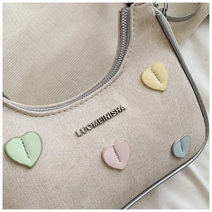 Close-up of beige canvas shoulder bag with silver logo and colorful stitched heart patches