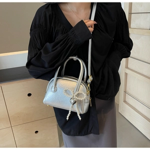 Vue détaillée du sac coquillage argenté avec nœud en perles et breloque cœur sur modèle