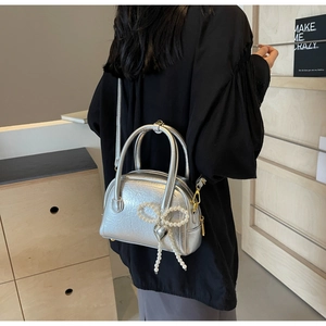 Détail du sac argenté plissé avec nœud en perles et breloque en métal en forme de cœur
