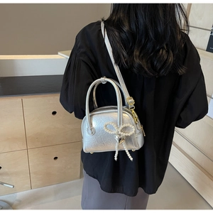 Détail d'un sac argenté texturé orné d'un nœud en perles et d'un pendentif cœur