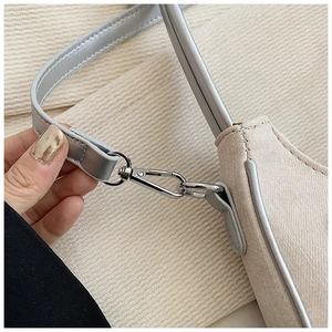 Detail of silver lobster clasp and grainy cream leather texture on the crossbody bag